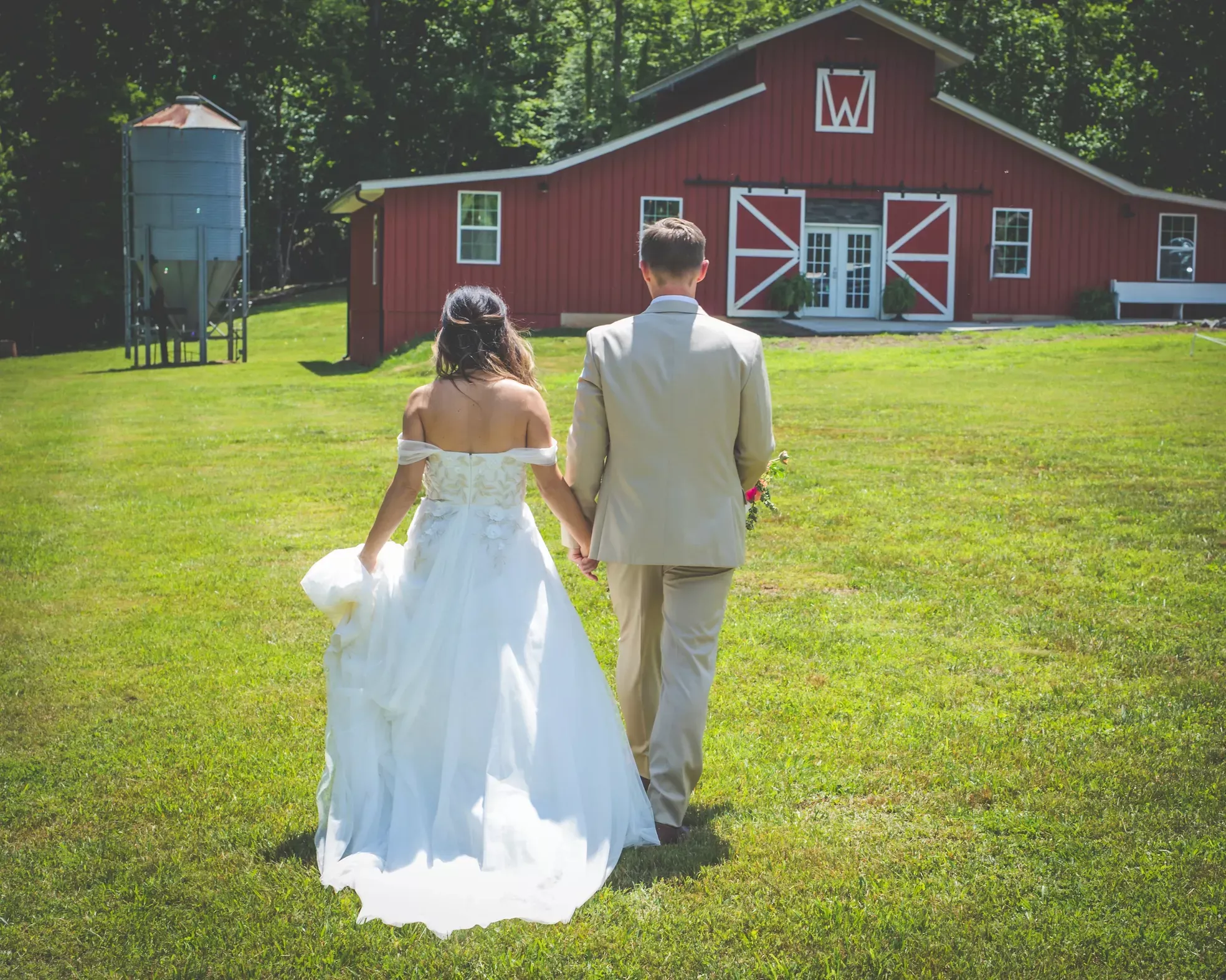 Couple at wedding in wedding dress and suit walking towards barn at Watkins Barn and Venue in Blue Ridge GA